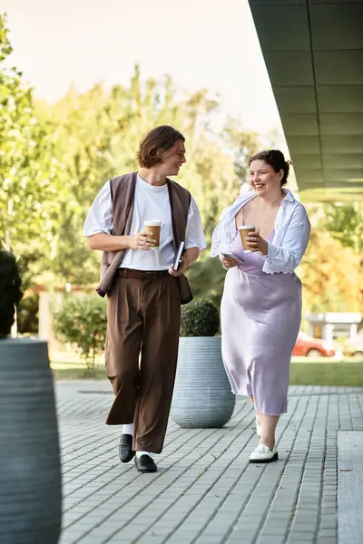 Two friends share a light hearted moment, sipping coffee while strolling outdoors. — Stock Photo