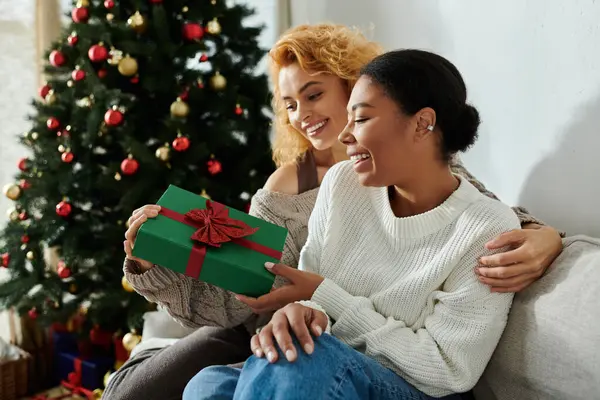 Two women exchange gifts at home, surrounded by a cheerful holiday atmosphere. — Stock Photo