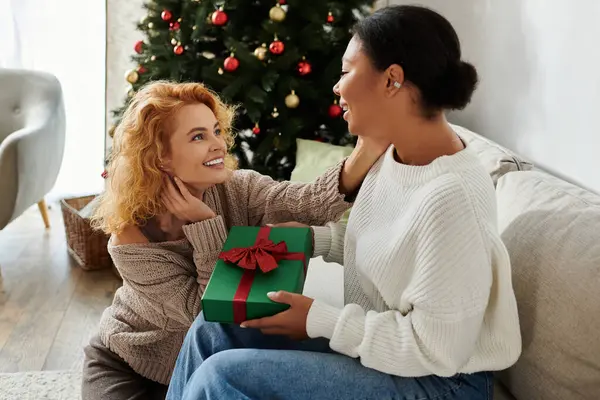Two women celebrate together at home, sharing laughter and a thoughtful gift during the holidays. — Stock Photo