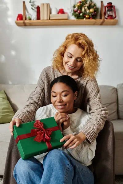 A couple enjoys joy as one gives the other a beautifully wrapped gift in their cozy living room. — Stock Photo