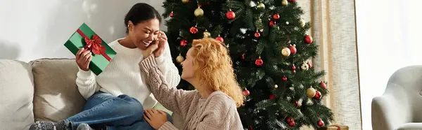 Una hermosa pareja de lesbianas comparte risas y amor mientras intercambian regalos en casa. — Stock Photo