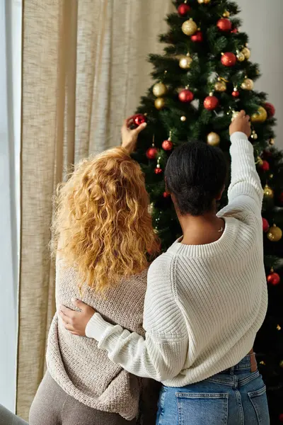 A loving couple joyfully adorns their Christmas tree with vibrant ornaments together. — Stock Photo