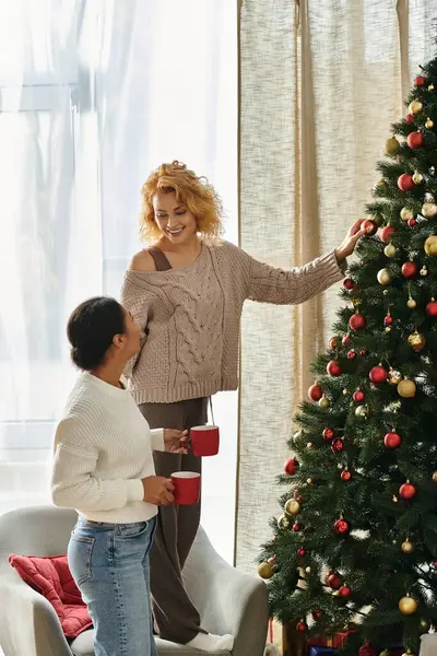 Two women brighten their home by decorating a Christmas tree together in joyful warmth. — Stock Photo