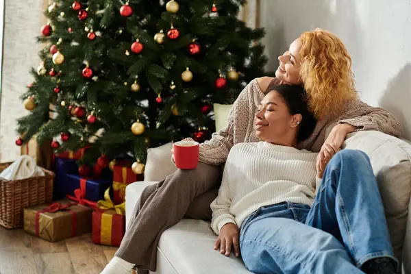 A loving couple enjoys a warm drink together by the festive Christmas tree. — Stock Photo