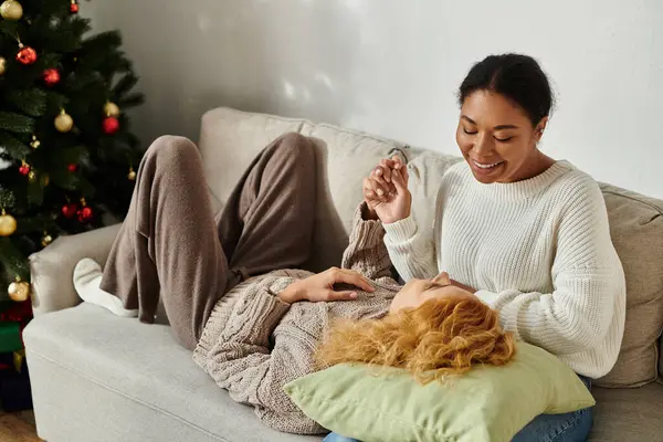 Zwei Frauen teilen Lachen und Wärme auf einer weichen Couch, umgeben von festlicher Dekoration. — Stockfoto