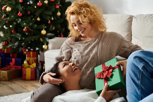 A joyful couple exchanges gifts and embraces while surrounded by holiday cheer at home. — Stock Photo