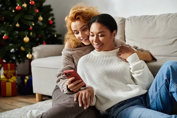 Two partners snuggle together on the couch, sharing smiles while looking at a phone. — Stock Photo
