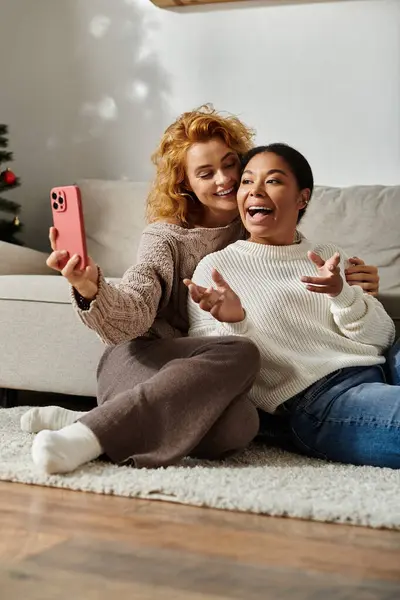 A joyful couple cuddles on the floor, capturing playful selfies in their cozy living room. — Stock Photo