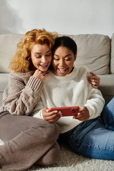 Zwei Frauen genießen fröhlich einen gemütlichen Abend und lachen zusammen, während sie etwas am Telefon beobachten. — Stockfoto