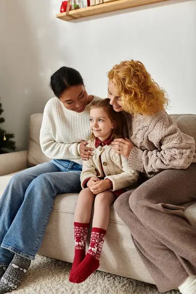 A joyful couple embraces their daughter on a cozy sofa, radiating warmth and love at home. — Stock Photo