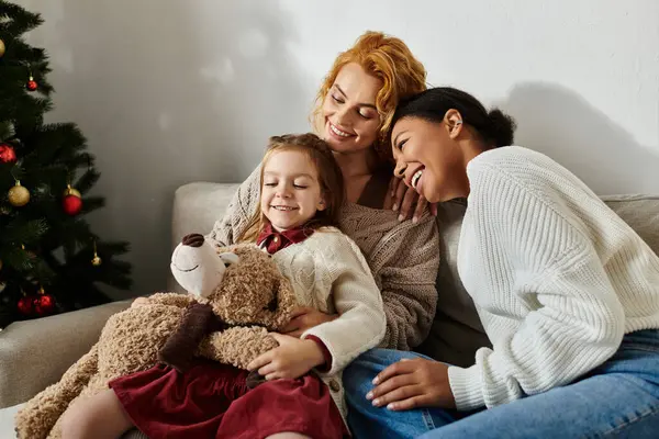 A joyful lesbian couple hugs their daughter at home, celebrating their loving family. — Stock Photo
