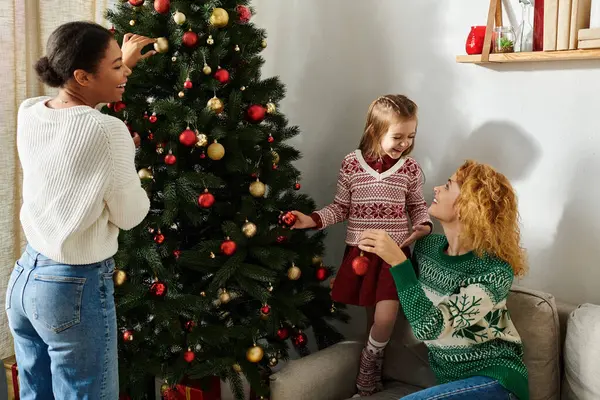 A loving couple and their daughter joyfully decorate their Christmas tree together. — Stock Photo