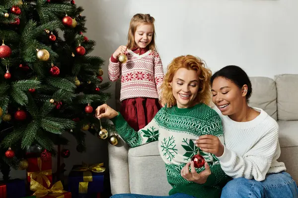 The family laughs together while adding ornaments to their Christmas tree at home. — Stock Photo
