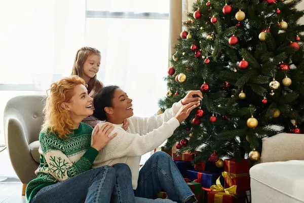 A loving couple and their daughter enjoy decorating a festive Christmas tree at home. — Stock Photo