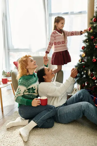 A loving couple shares laughter as their daughter adorns the Christmas tree with joy. — Stock Photo