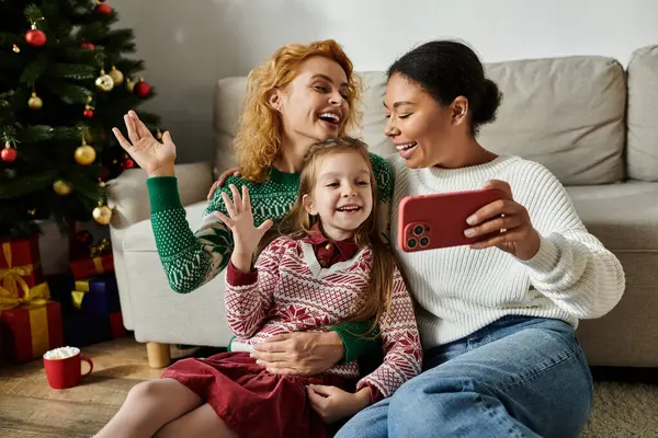 A loving couple shares laughter with their daughter while capturing holiday memories at home. — Stock Photo