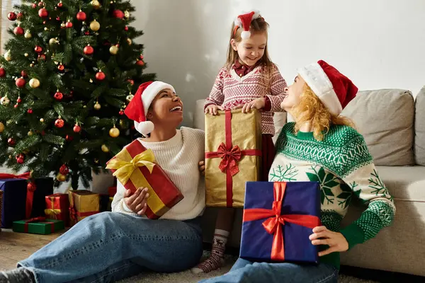A loving couple shares a delightful moment with their daughter as they exchange gifts at home. — Stock Photo