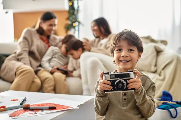 A smiling boy holds a camera while his family enjoys the festive spirit in their modern living room. — Stock Photo