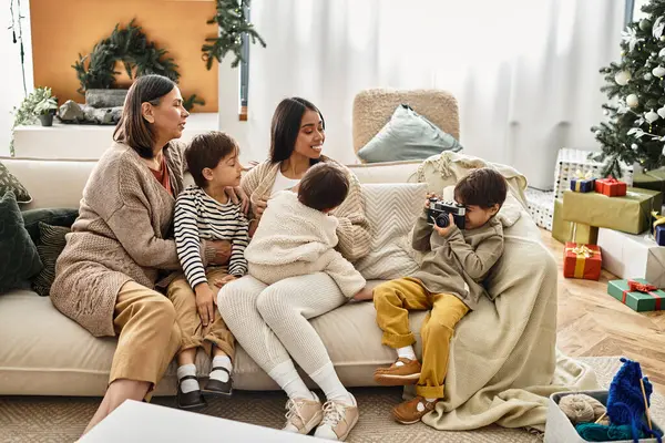 Ein asiatischer Junge fotografiert die Familie, während er sich freudig in ihrem modernen Wohnzimmer an einem schön geschmückten Weihnachtsbaum versammelt. — Stockfoto