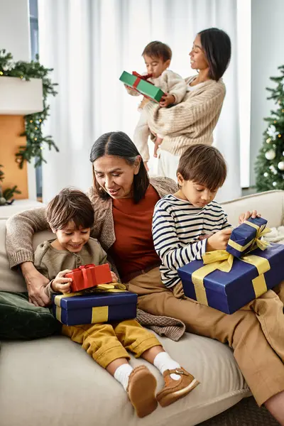 A joyful gathering of an Asian family as they celebrate Christmas while unwrapping gifts by the tree. — Stock Photo
