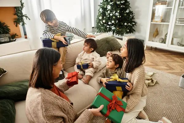 An Asian family shares joyful moments by the Christmas tree, exchanging gifts during the festive winter holidays. — Stock Photo