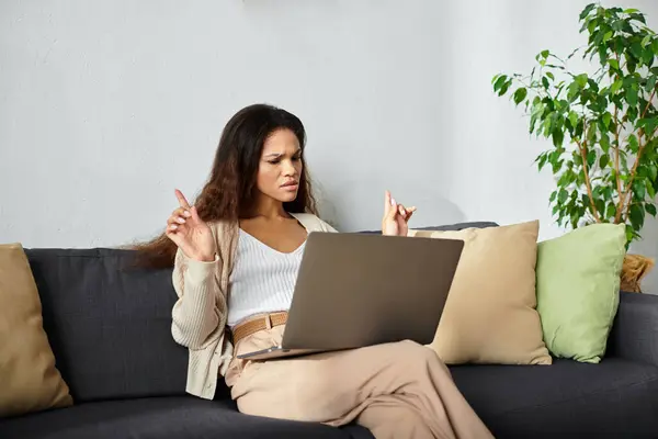 A woman sits on a couch, intently working on her laptop in a serene and inviting space. — Stock Photo