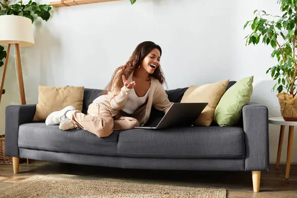 La femme se prélasse confortablement sur un canapé, souriante et animée alors qu'elle discute en ligne. — Photo de stock