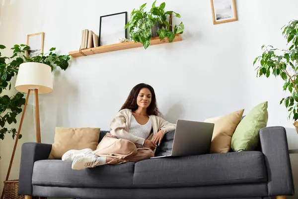 The woman enjoys a calm moment, working on her laptop surrounded by lush plants and soft cushions. — Stock Photo