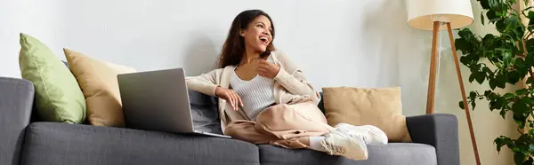 The cheerful woman lounges comfortably on a stylish couch, savoring a delightful moment. — Stock Photo
