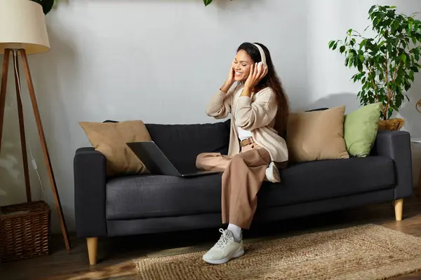 A joyful woman listens to music with headphones while seated comfortably on a sofa. — Stock Photo