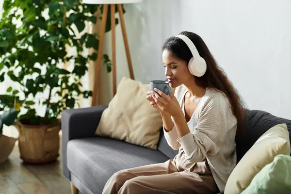A woman in headphones savors a warm beverage, enveloped in a tranquil atmosphere at home. — Stock Photo