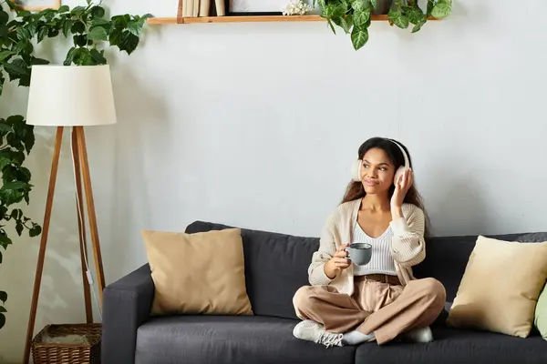 Une femme s'assoit paisiblement sur le canapé, dégustant son thé tout en écoutant de la musique. — Photo de stock