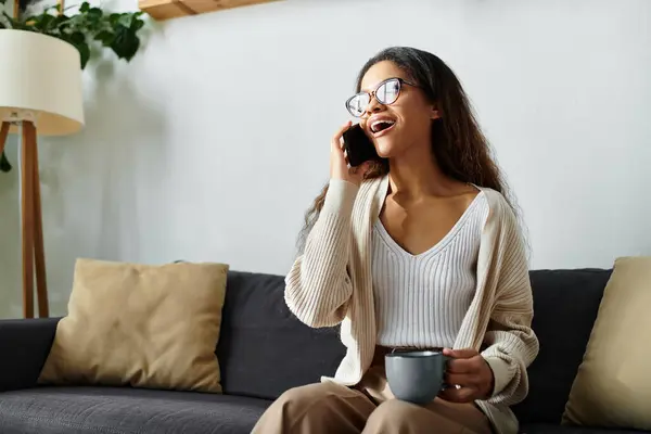 Bright sunlight fills the cozy room as a woman laughs brightly, holding her coffee and phone. — Stock Photo