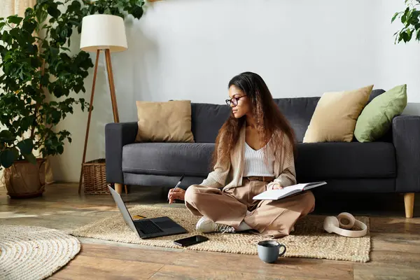 The woman sits comfortably on the floor, focused on her notebook while surrounded by greenery. — Stock Photo