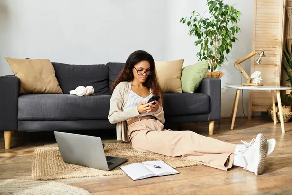 Une femme s'assoit confortablement sur le sol, engagée avec son appareil mobile dans un espace serein. — Photo de stock