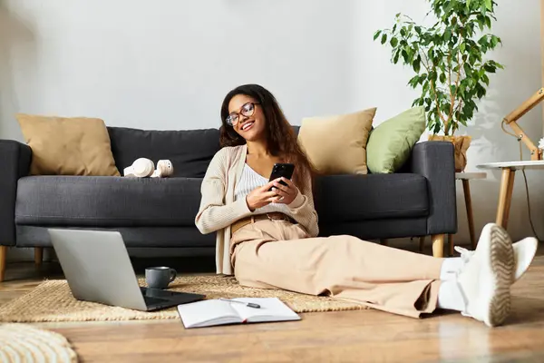 She enjoys her time on the floor, surrounded by comfort, with her phone in hand. — Stock Photo