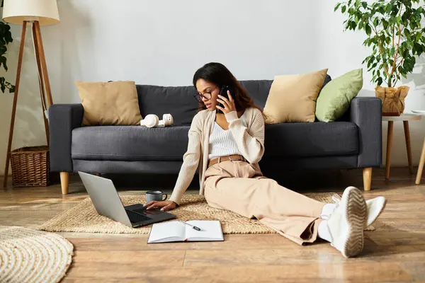 Seduto sul pavimento, una donna multitasking facendo una chiamata e digitando sul suo computer portatile. — Foto stock