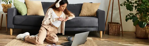 Seated comfortably on the floor, a woman explores her laptop with interest in a cozy space. — Stock Photo