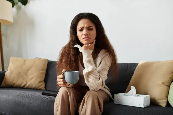 A curly haired woman sits on a couch, sipping tea and lost in thought. — Stock Photo