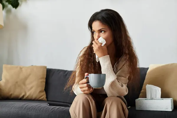A young woman with long hair holds a mug, looking pensive while feeling under the weather. — Stock Photo