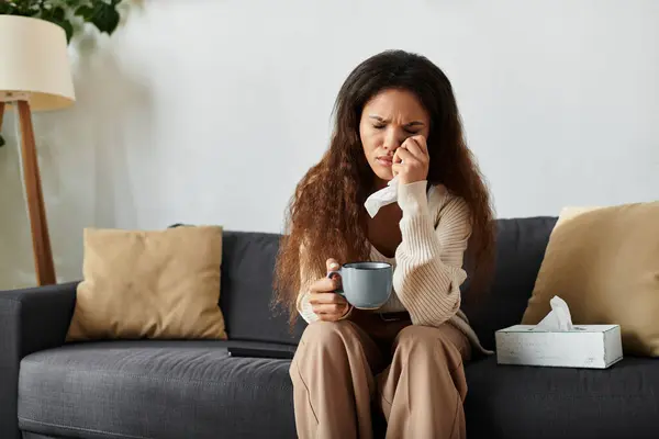 Eine Frau sitzt auf einem Sofa, hält einen Becher in der Hand und betrachtet ihre Gedanken inmitten einer heiteren Atmosphäre. — Stockfoto