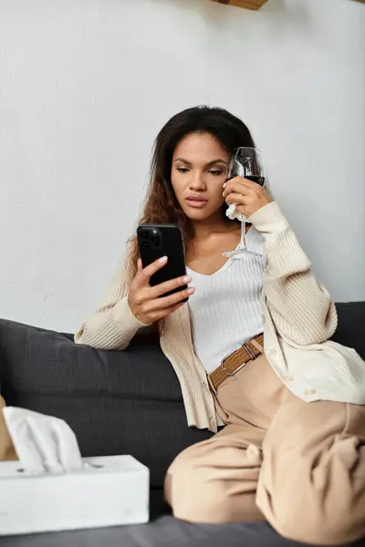 A fashionable woman lounges comfortably, holding a glass of wine and looking at her phone. — Stock Photo