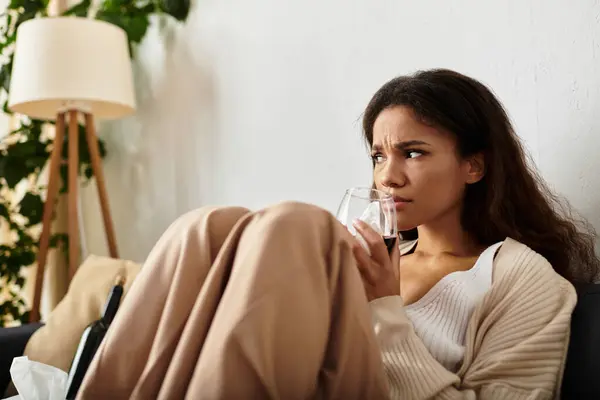 Profondément réfléchie, une femme s'assoit confortablement, sirotant une boisson enveloppée dans des vêtements chauds. — Photo de stock