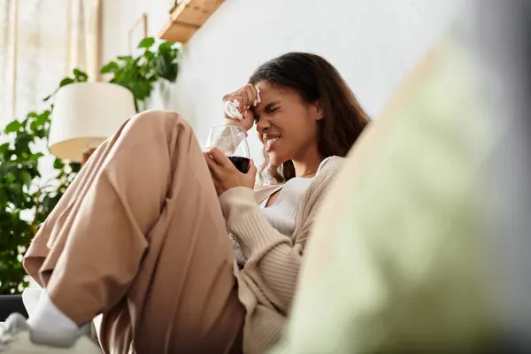 A thoughtful woman sits comfortably on a couch, sipping a drink in a bright, serene space. — Stock Photo
