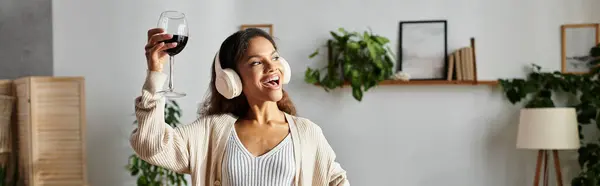 Eine Frau hebt freudig ein Glas Wein in die Höhe und umarmt die gemütliche Atmosphäre zu Hause. — Stock Photo