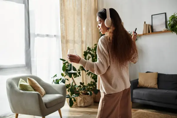 A woman dances with headphones and wine in a bright, plant filled room. — Stock Photo