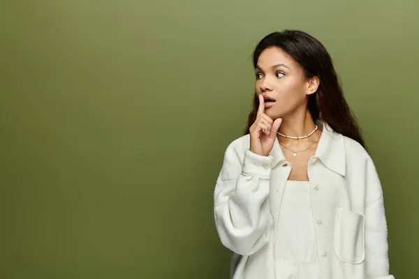 A beautiful woman holds her finger to her lips, suggesting silence, amidst a soft green backdrop. — Stock Photo