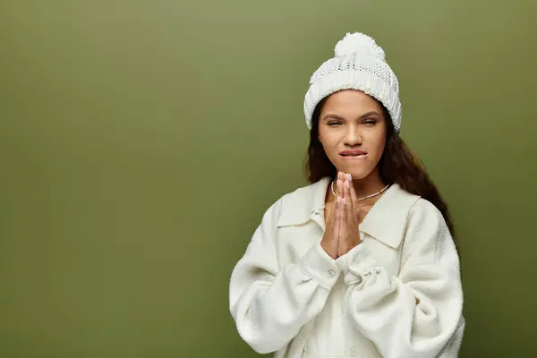 A woman in a white sweater and hat looks thoughtful while standing against a green wall. — Stock Photo