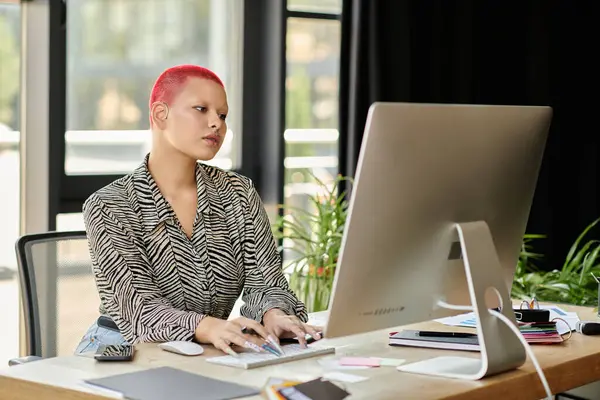 A stylish bald woman focuses on her computer while surrounded by greenery and office supplies. — Stock Photo