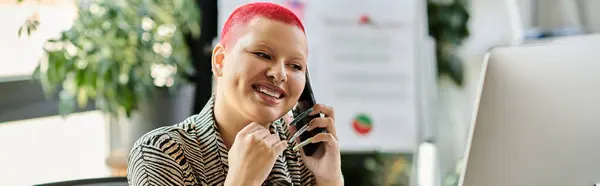 A bald woman with vibrant pink hair is engaged in a cheerful phone conversation while working. — Stock Photo